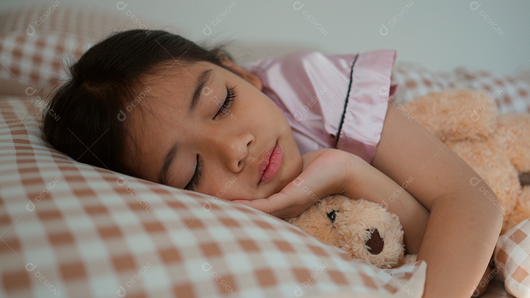 Linda menina dormindo sobre sua cama abraçando seu ursinho de pelúcia