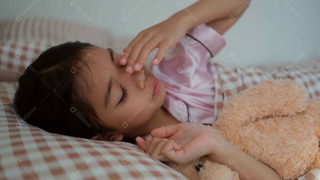 Linda menina dormindo sobre sua cama abraçando seu ursinho de pelúcia