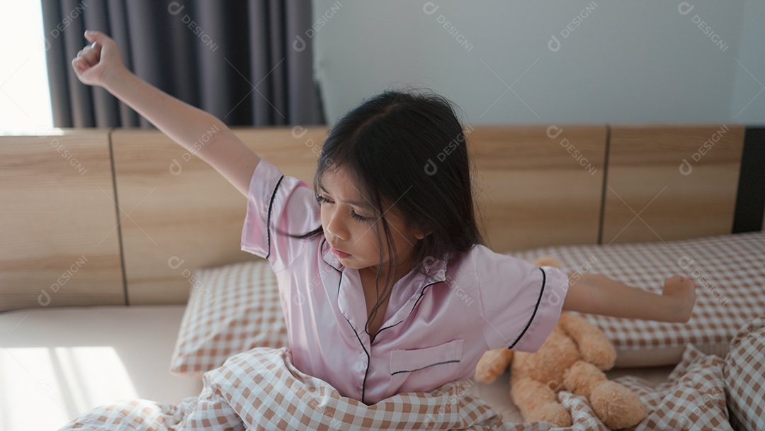 Linda menina acordando sobre sua cama ao lado do seu ursinho de pelúcia