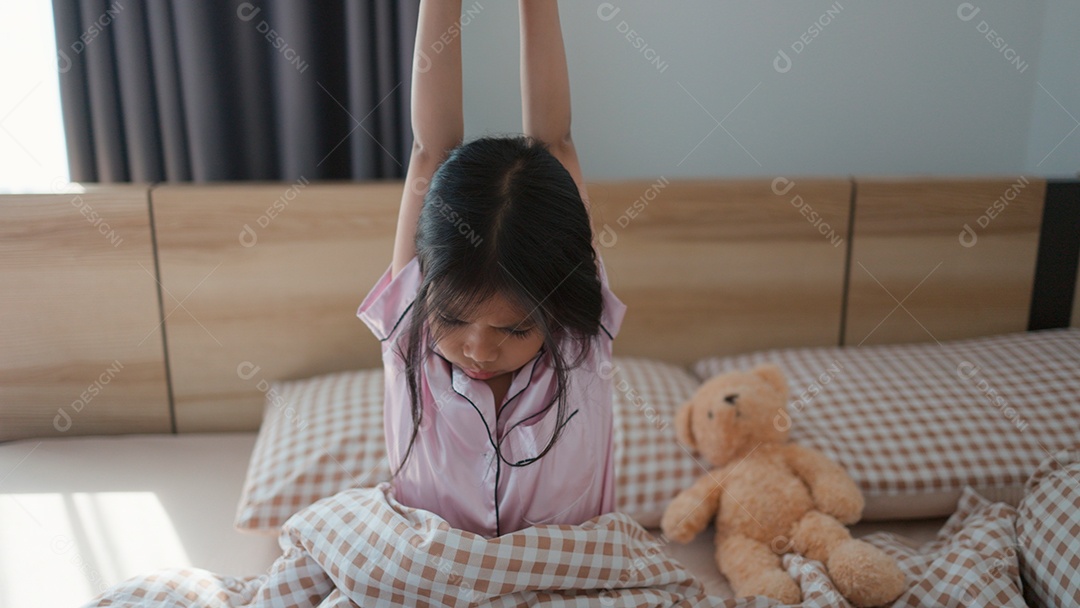 Linda menina acordando sobre sua cama ao lado do seu ursinho de pelúcia