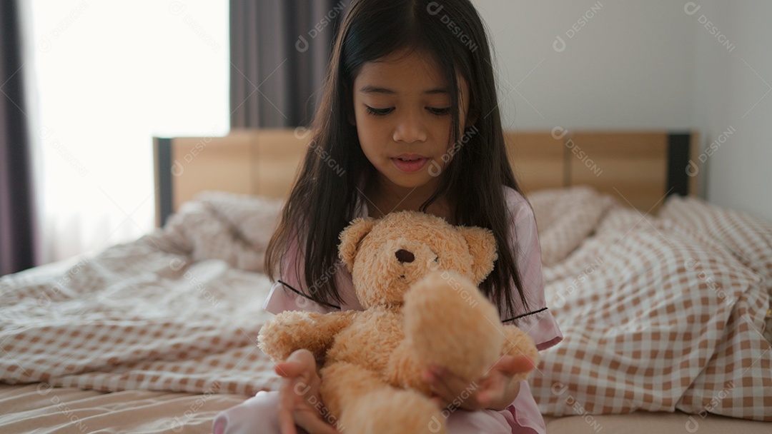 Linda menina sentada sobre sua cama segurando seu ursinho de pelúcia