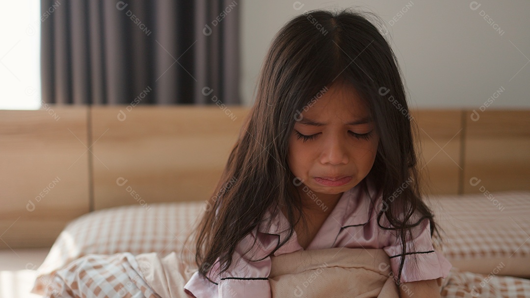 Linda menina assustada no quarto chorando com as mãos segurando seu ursinho com medo sobre fundo desfocado