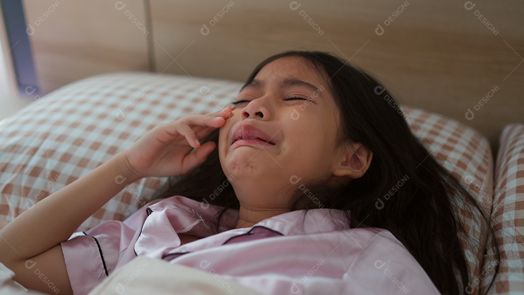 Linda menina acordando assustada sobre sua cama ao lado do seu ursinho de pelúcia