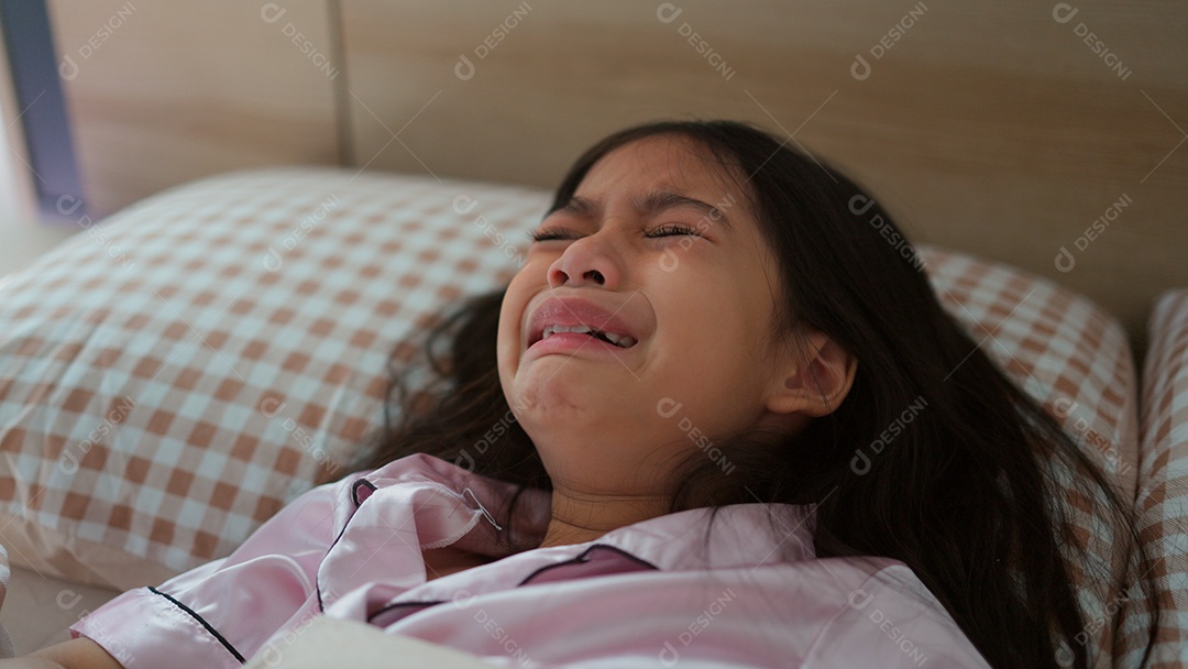 Linda menina acordando assustada sobre sua cama ao lado do seu ursinho de pelúcia