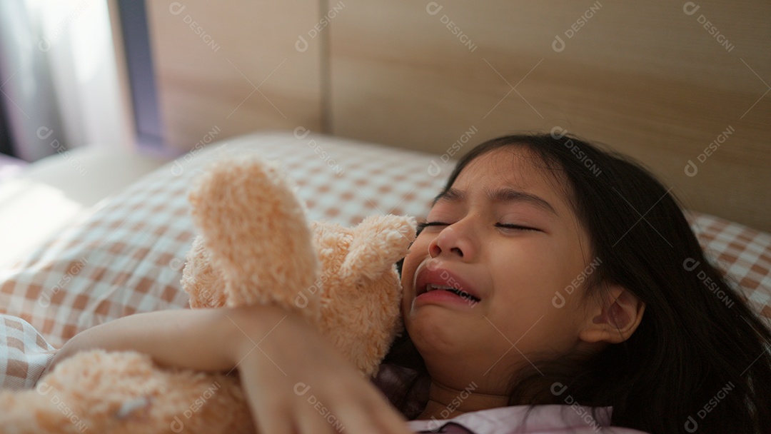 Linda menina acordando assustada abraçando seu ursinho de pelúcia sobre sua cama