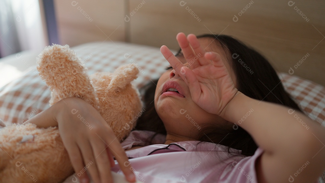 Linda menina acordando assustada abraçando seu ursinho de pelúcia sobre sua cama