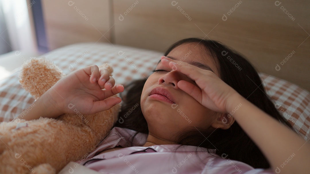 Linda menina acordando assustada abraçando seu ursinho de pelúcia sobre sua cama