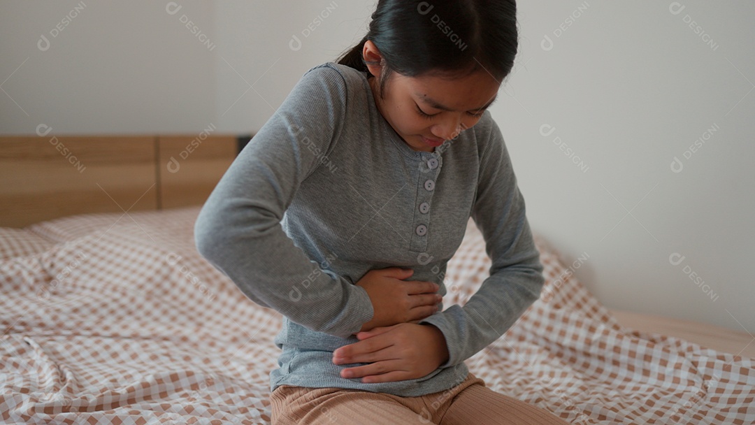 Linda menina sentada sobre sua cama com dor desagradável na barriga
