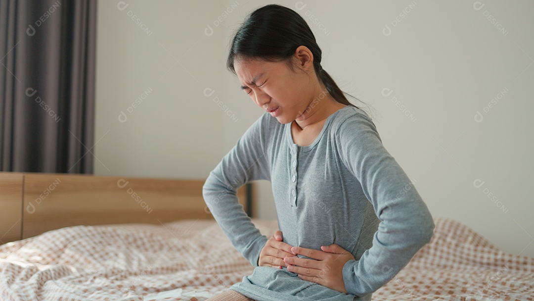 Linda menina sentada sobre sua cama com dor desagradável na barriga