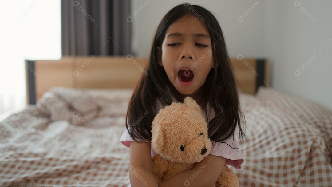 Linda menina sentada sobre sua cama segurando seu ursinho de pelúcia