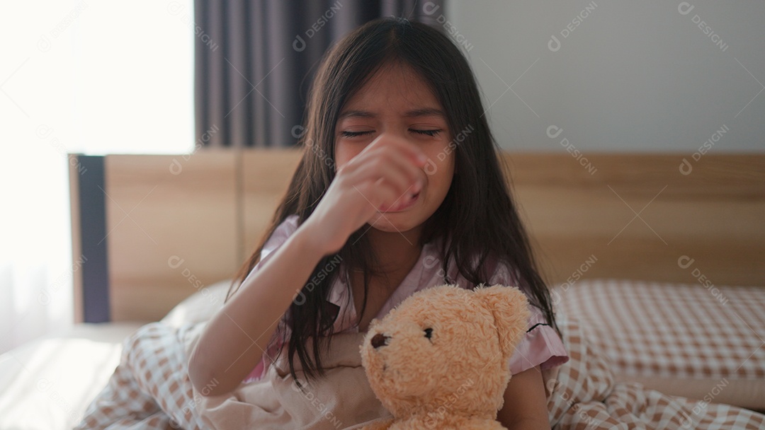 Linda menina sentada sobre sua cama assustada segurando seu ursinho de pelúcia