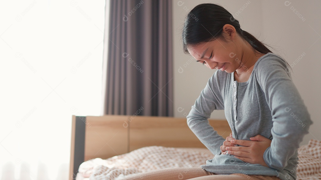 Linda menina sentada sobre sua cama com dor desagradável na barriga