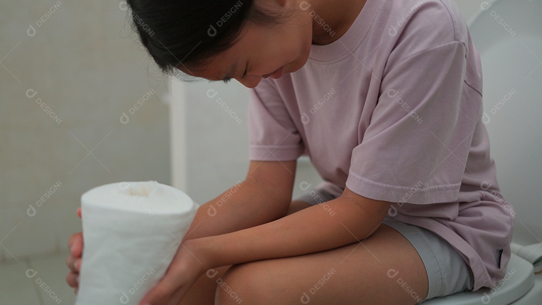 Linda menina asiática sentada em vaso sanitário segurando papel higiênico