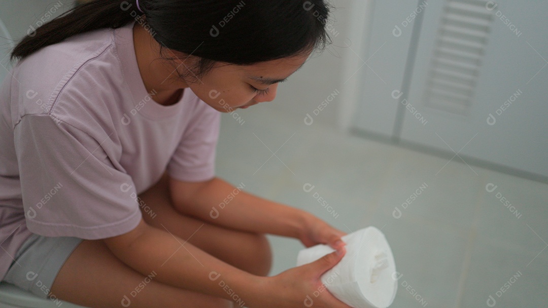 Linda menina asiática sentada em vaso sanitário segurando papel higiênico