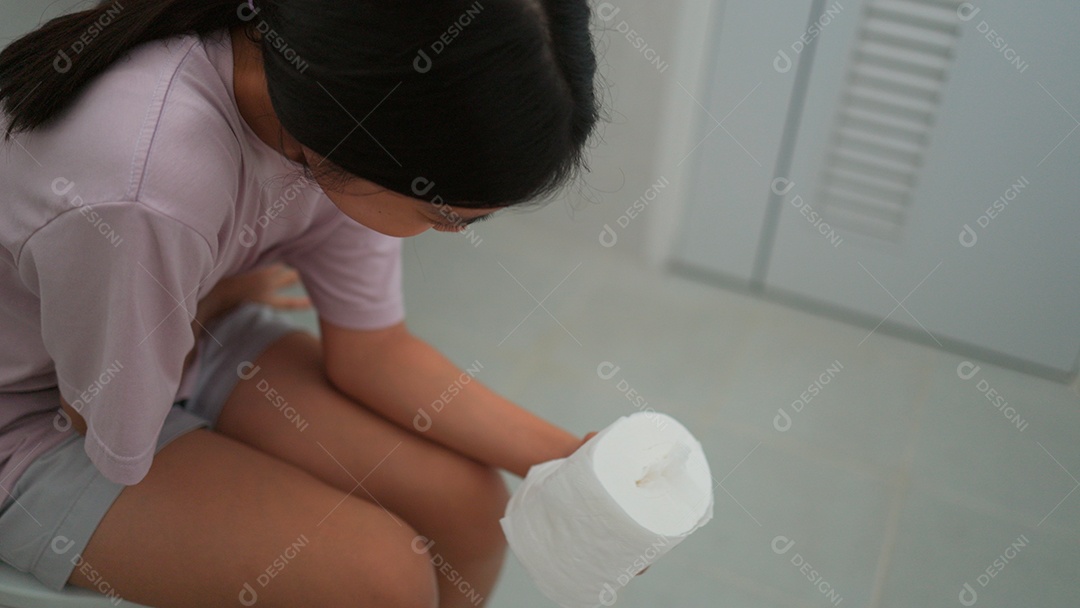 Linda menina asiática sentada em vaso sanitário segurando papel higiênico