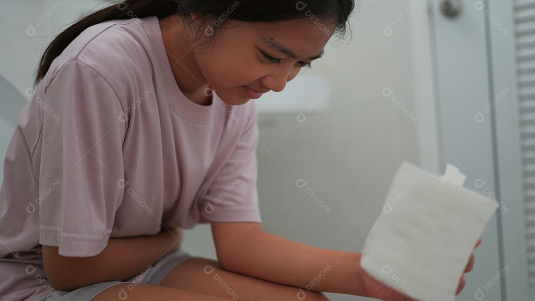 Linda menina asiática sentada em vaso sanitário segurando papel higiênico