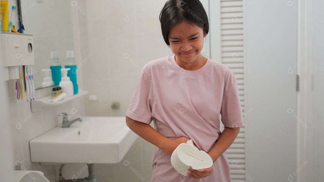 Linda menina asiática  em pé segurando papel higiênico com fortes dores na barriga