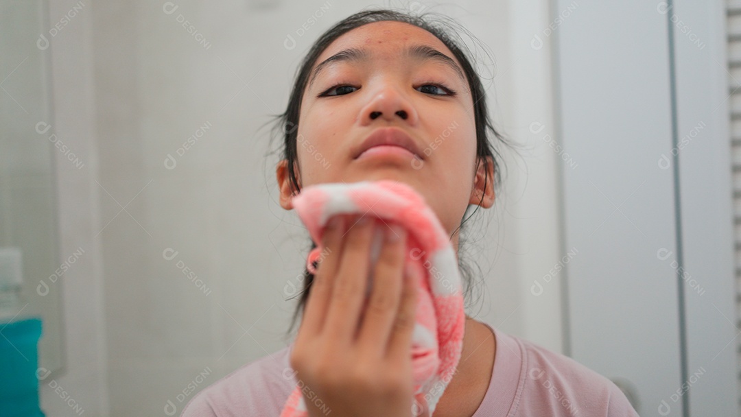 Linda menina asiática enfrente ao espelho enxugando o rosto