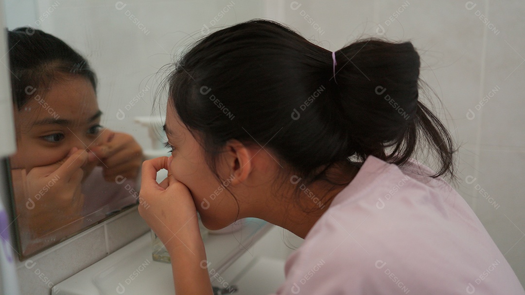 Linda menina asiática enfrente ao espelho espremendo espinha do rosto