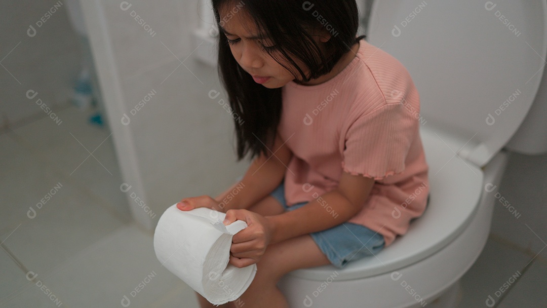 Linda menina asiática sentada em vaso sanitário segurando papel higiênico com dor de barriga