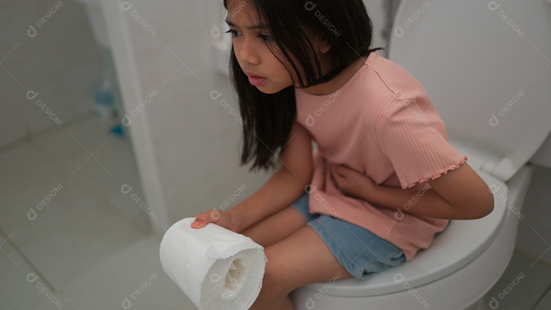 Linda menina asiática sentada em vaso sanitário segurando papel higiênico com dor de barriga