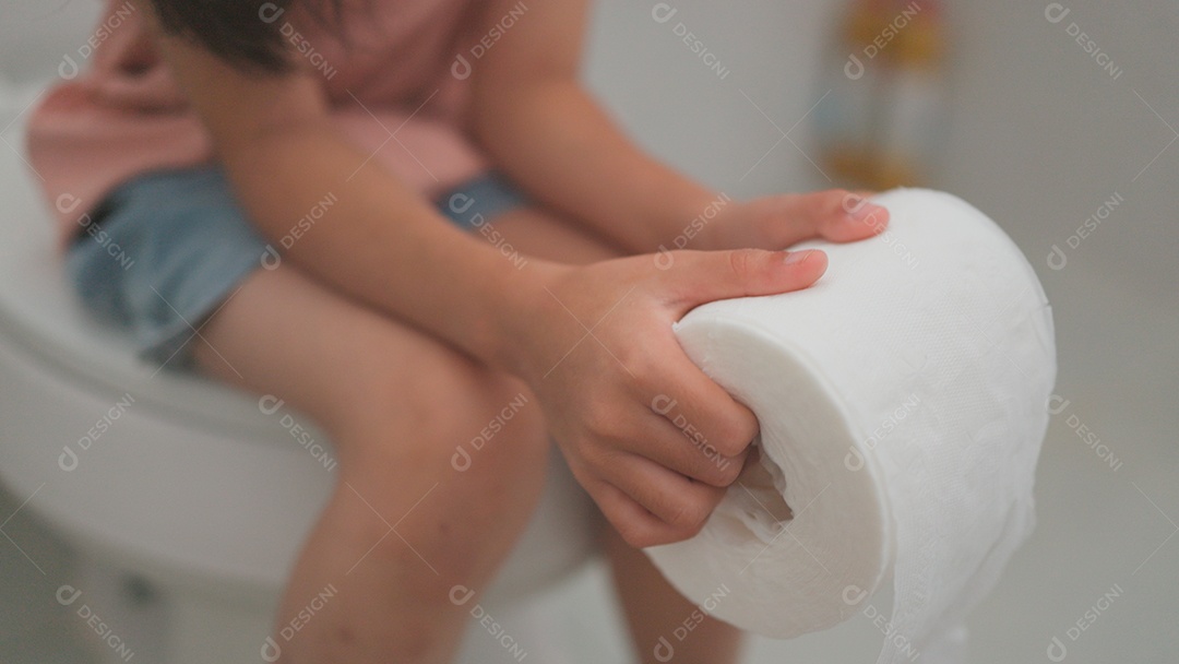 Linda menina asiática sentada em vaso sanitário segurando papel higiênico com dor de barriga