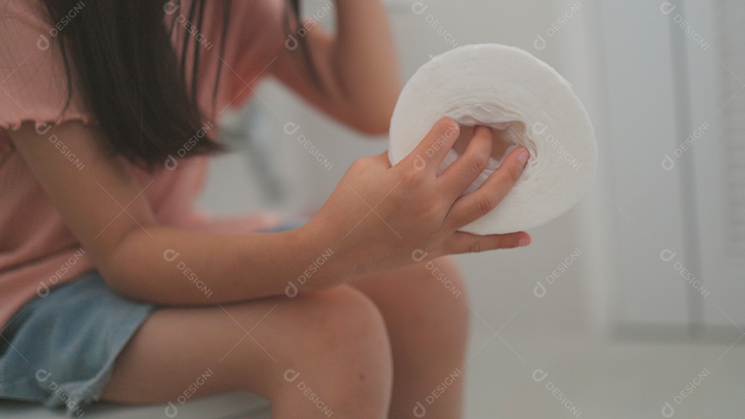 Linda menina asiática sentada em vaso sanitário segurando papel higiênico com dor de barriga