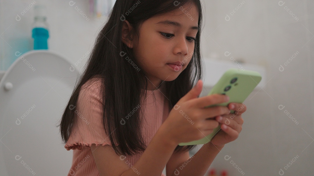 Linda menina asiática sentada em vaso sanitário mechendo em smartphone