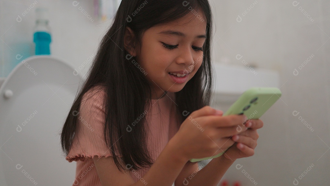 Linda menina asiática sentada em vaso sanitário mechendo em smartphone