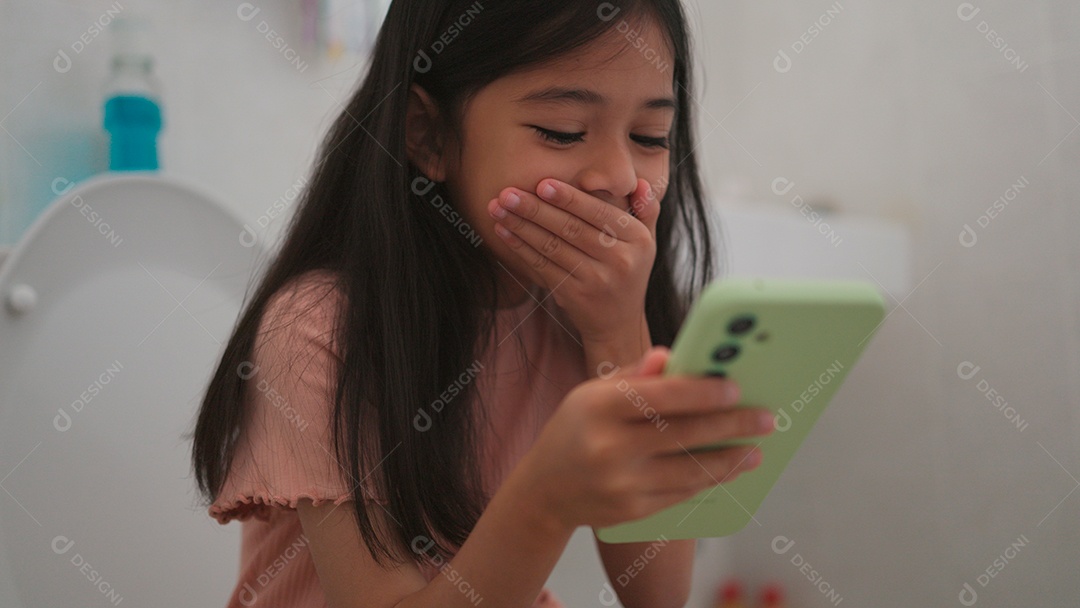 Linda menina asiática sentada em vaso sanitário mechendo em smartphone
