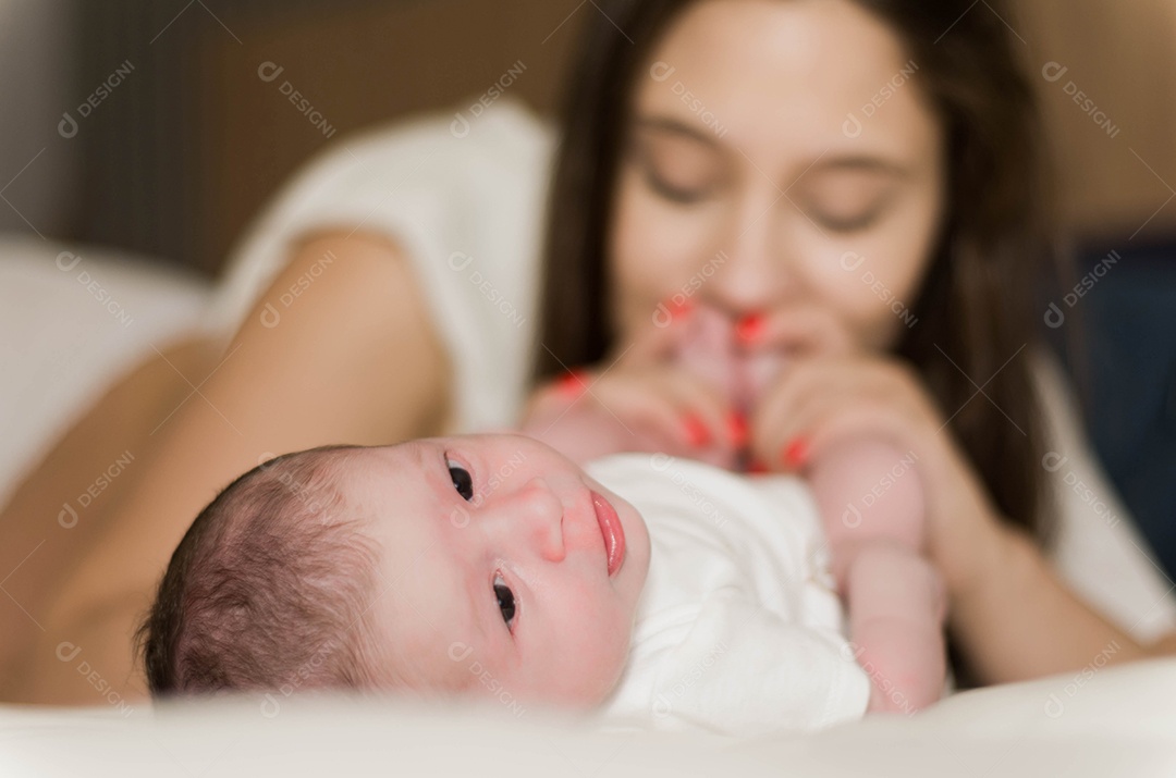 Jovem mãe carinhosa brincando com seu filho recém nascido na cama