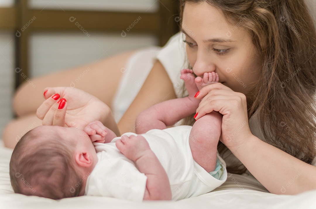 Jovem mãe carinhosa brincando com seu filho recém nascido na cama