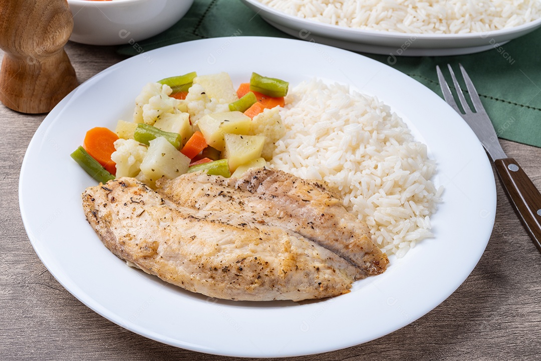 A imagem mostra um prato de filé de peixe grelhado servido com arroz branco e legumes cozidos no vapor.