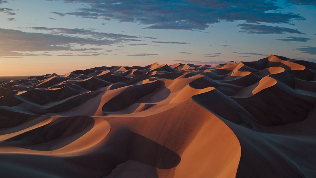 Uma paisagem desértica dramática com altas dunas de areia e sombras mudando conforme o sol se põe.