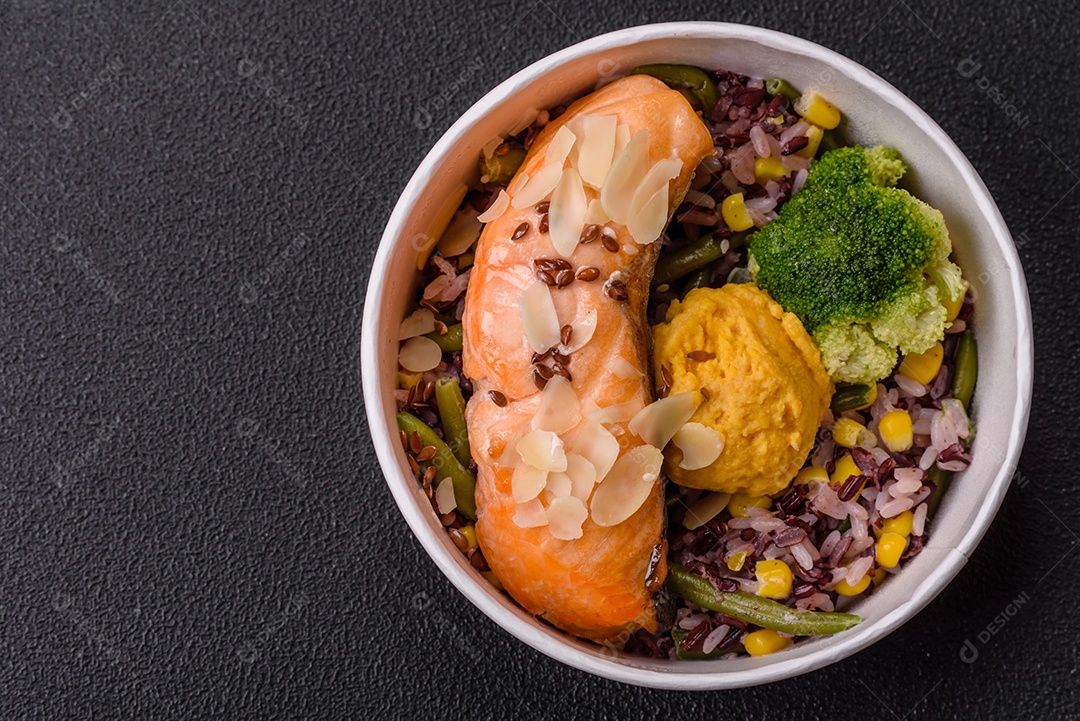 Um pedaço de salmão cozido com arroz, brócolis, sal e especiarias em um fundo de concreto escuro