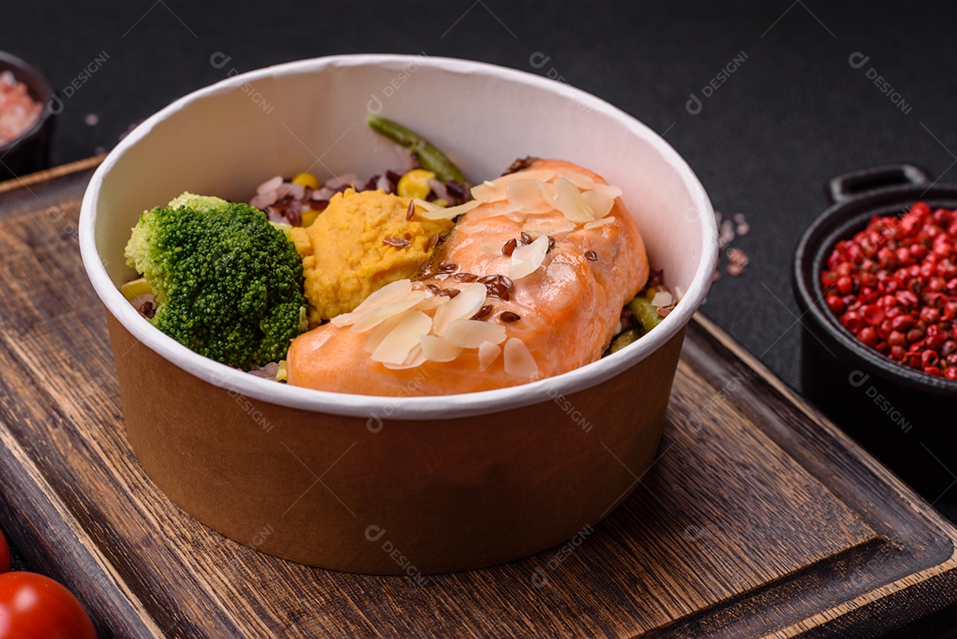 Um pedaço de salmão cozido com arroz, brócolis, sal e especiarias em um fundo de concreto escuro