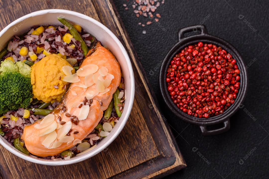Um pedaço de salmão cozido com arroz, brócolis, sal e especiarias em um fundo de concreto escuro