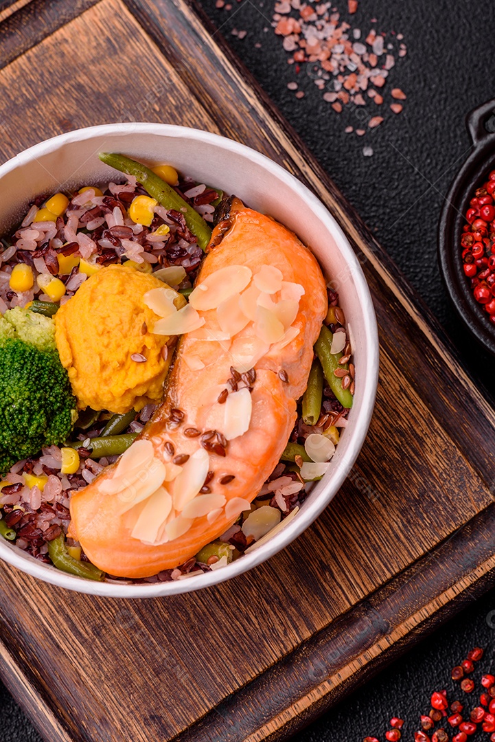 Um pedaço de salmão cozido com arroz, brócolis, sal e especiarias em um fundo de concreto escuro