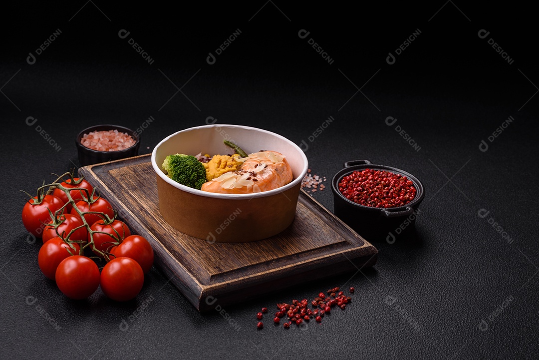 Um pedaço de salmão cozido com arroz, brócolis, sal e especiarias em um fundo de concreto escuro