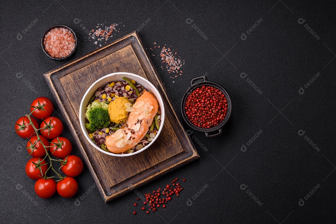 Um pedaço de salmão cozido com arroz, brócolis, sal e especiarias em um fundo de concreto escuro