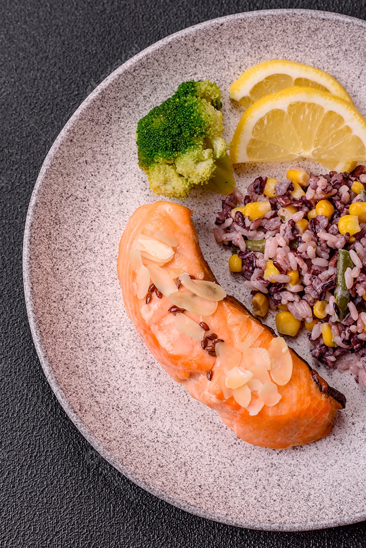 Um pedaço de salmão cozido com arroz, brócolis, sal e especiarias em um fundo de concreto escuro