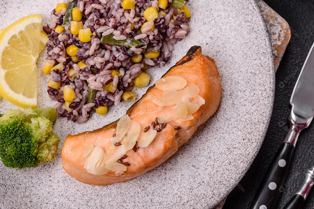 Um pedaço de salmão cozido com arroz, brócolis, sal e especiarias em um fundo de concreto escuro