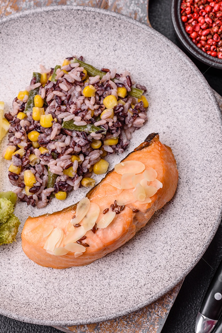 Um pedaço de salmão cozido com arroz, brócolis, sal e especiarias em um fundo de concreto escuro