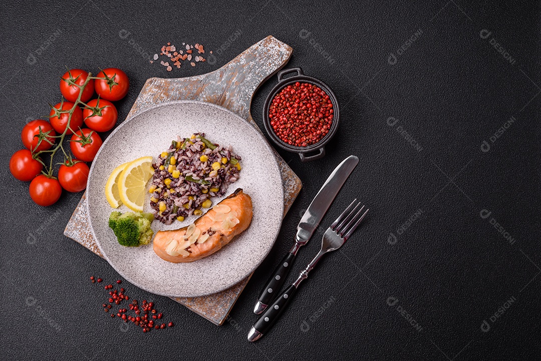 Um pedaço de salmão cozido com arroz, brócolis, sal e especiarias em um fundo de concreto escuro