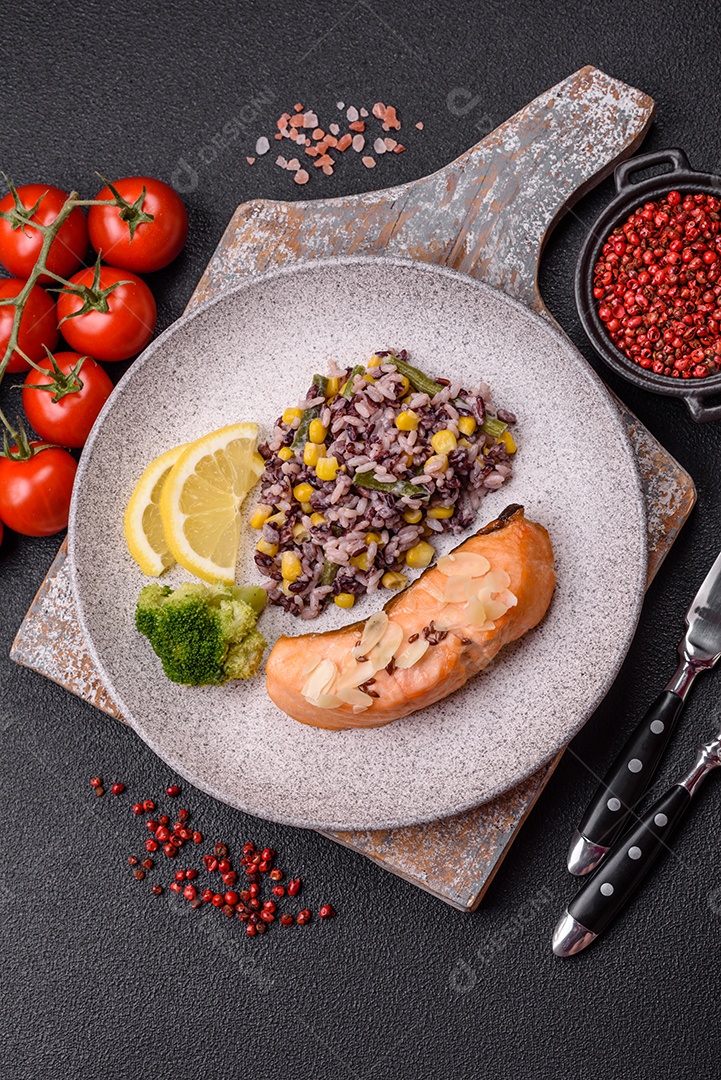 Um pedaço de salmão cozido com arroz, brócolis, sal e especiarias em um fundo de concreto escuro