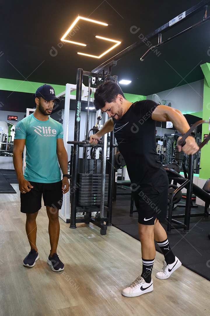 Belo personal trainer ajudando homem executar exercícios sobre uma academia