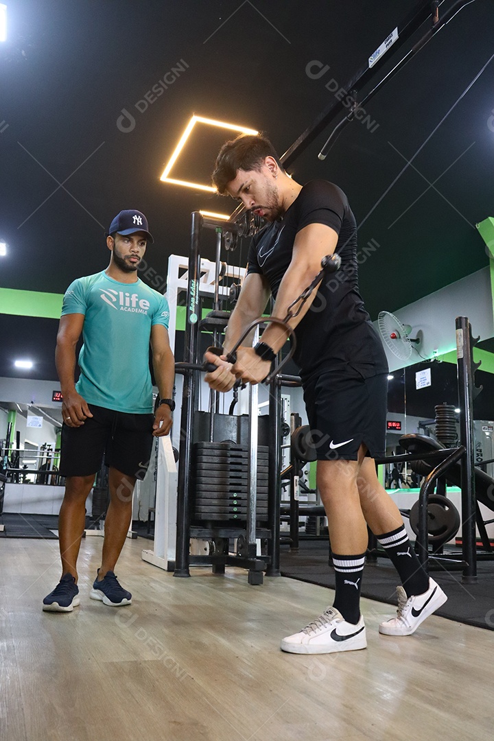 Belo personal trainer ajudando homem executar exercícios sobre uma academia