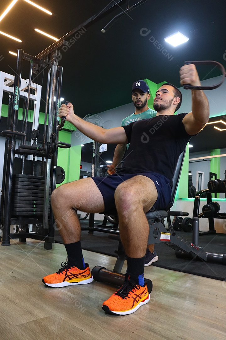 Belo personal trainer ajudando homem executar exercícios sobre uma academia