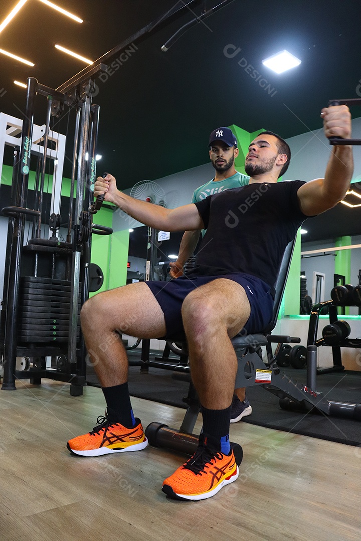 Belo personal trainer ajudando homem executar exercícios sobre uma academia