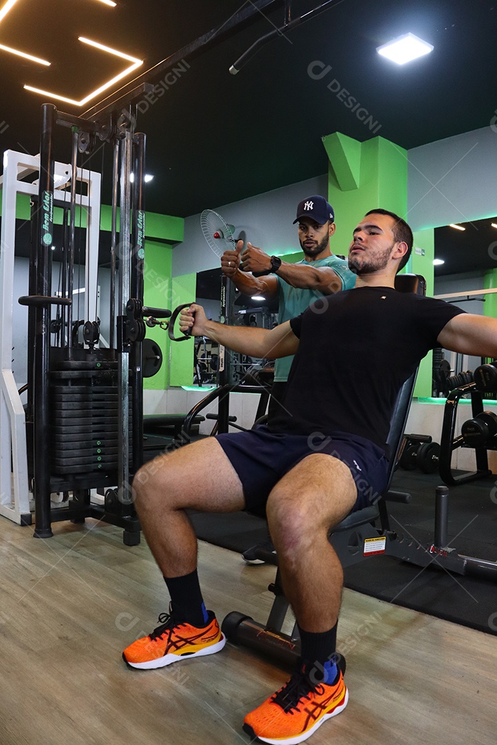 Belo personal trainer ajudando homem executar exercícios sobre uma academia